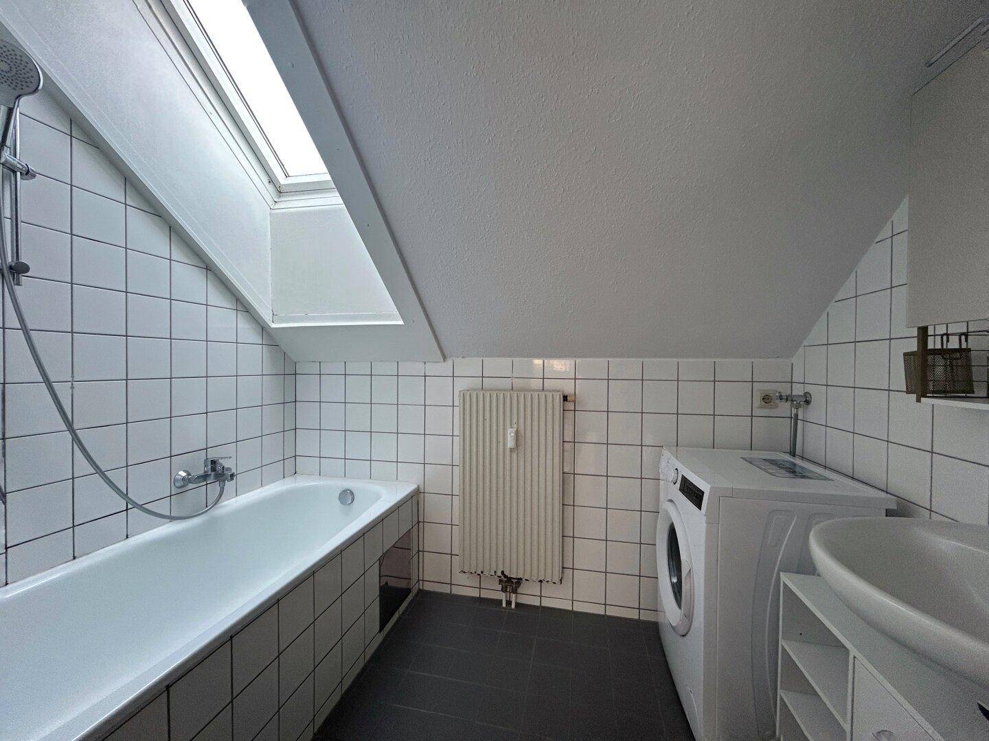 Modern gefliestes Badezimmer mit Badewanne, Dusche, Waschmaschine und Dachfenster.