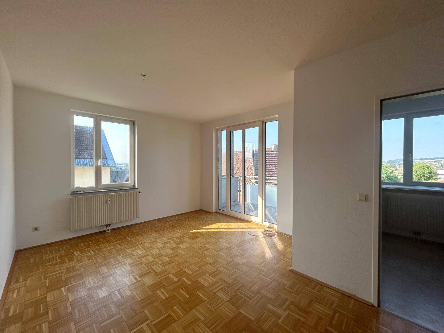 Geräumiges Wohnzimmer mit Parkettboden, großen Fenstern und direktem Zugang zum Balkon.