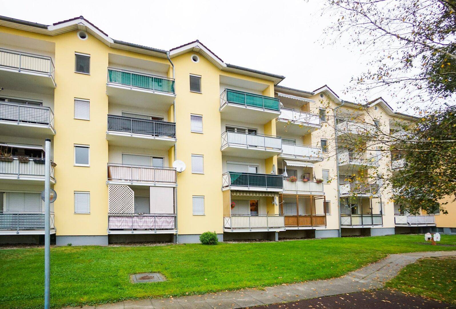 Mehrfamilienhaus mit gelber Fassade, vielen Balkonen und Grünflächen davor.