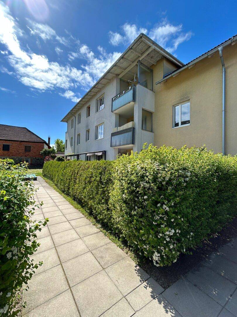 Mehrstöckiges Wohngebäude mit Balkonen, umgeben von einer gepflegten Hecke und einem Gehweg.