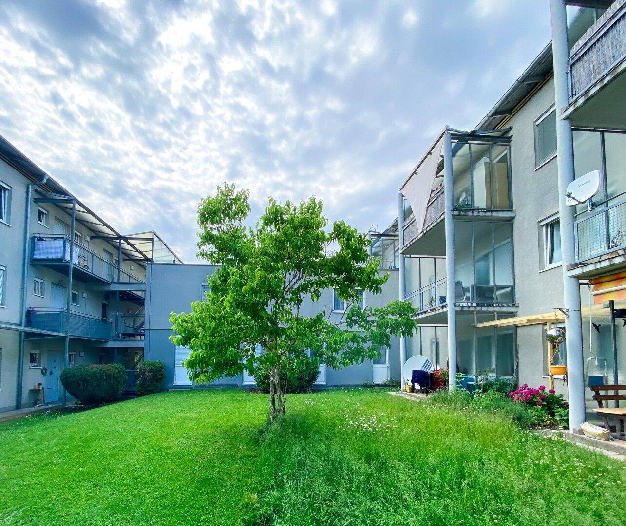 Mehrfamilienhaus mit mehreren Balkonen und einer gepflegten Grünfläche im Vordergrund unter bewölktem Himmel.