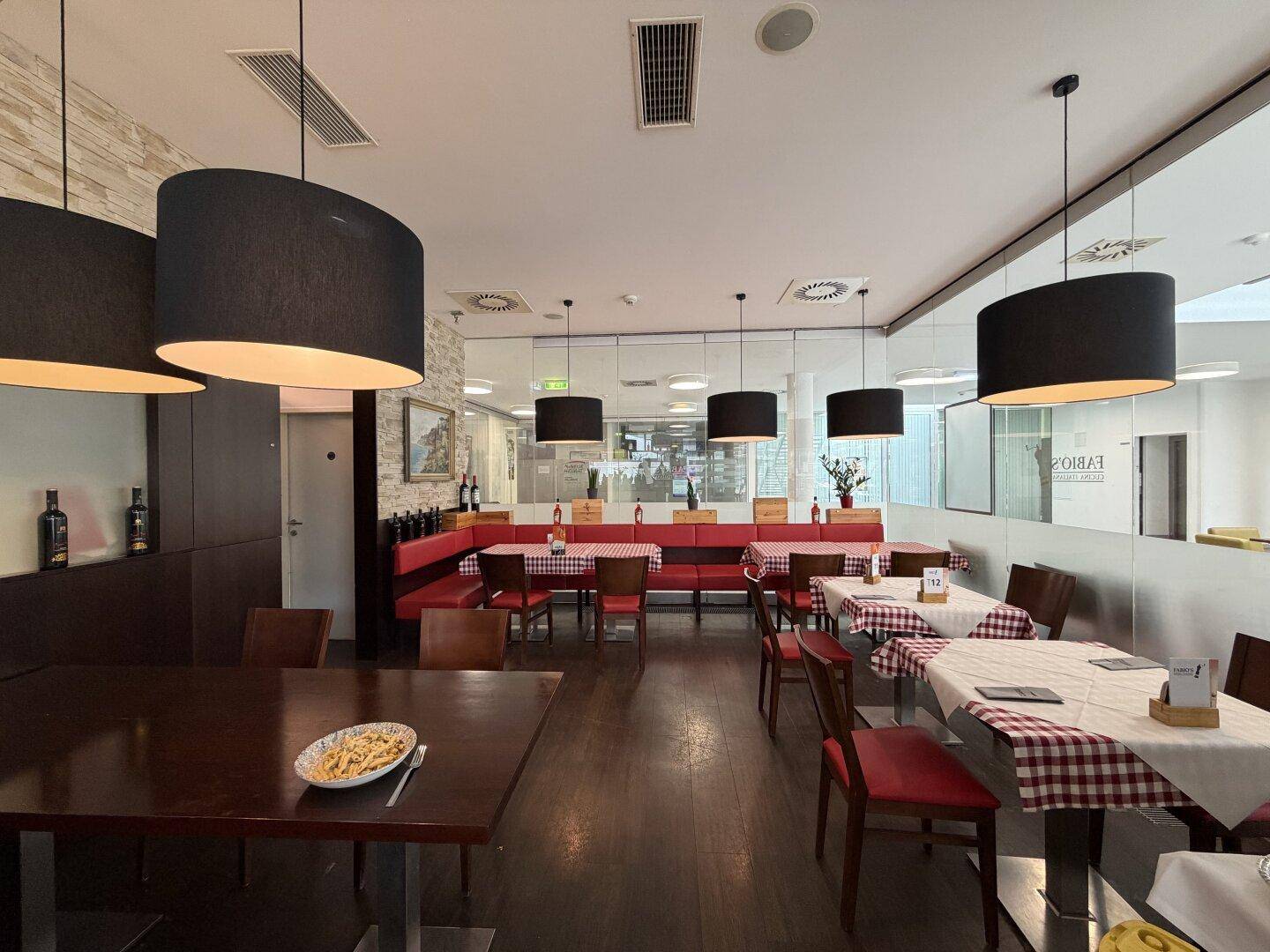 Gemütlicher Restaurantbereich mit roten Sitzbänken, Holztischen und karierten Tischdecken.