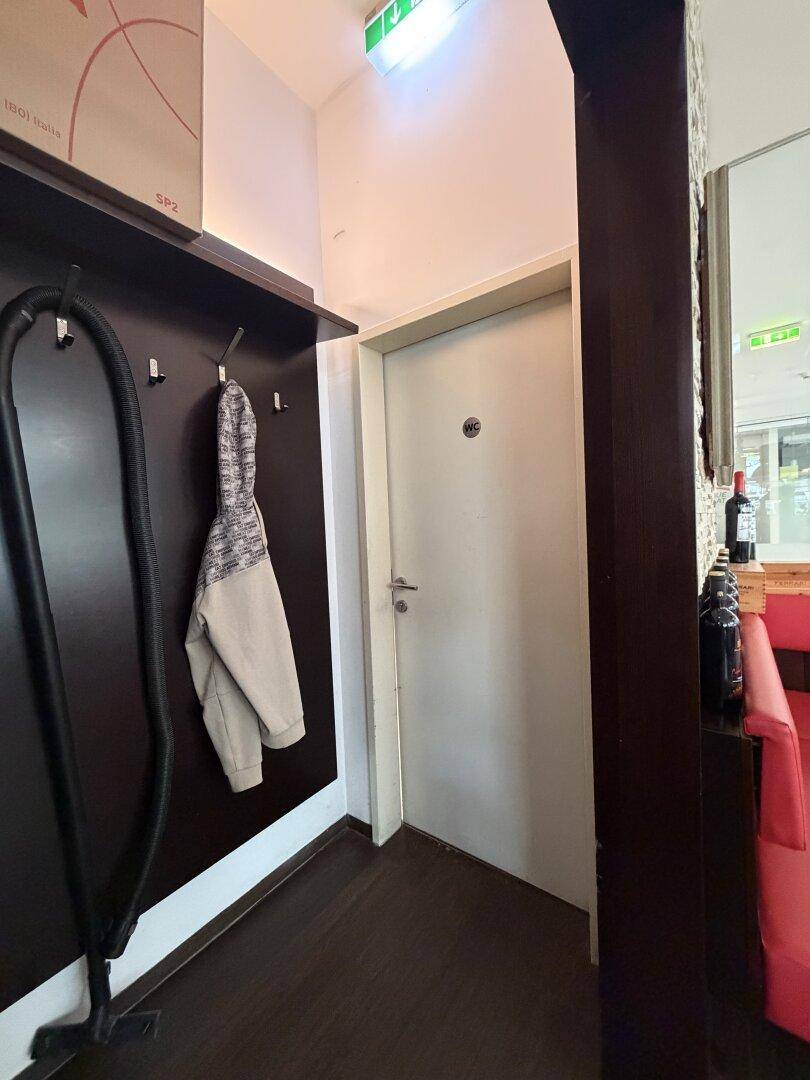 Schmaler Flur mit Garderobe und einer schlichten weißen Tür, die zu einem weiteren Raum führt.