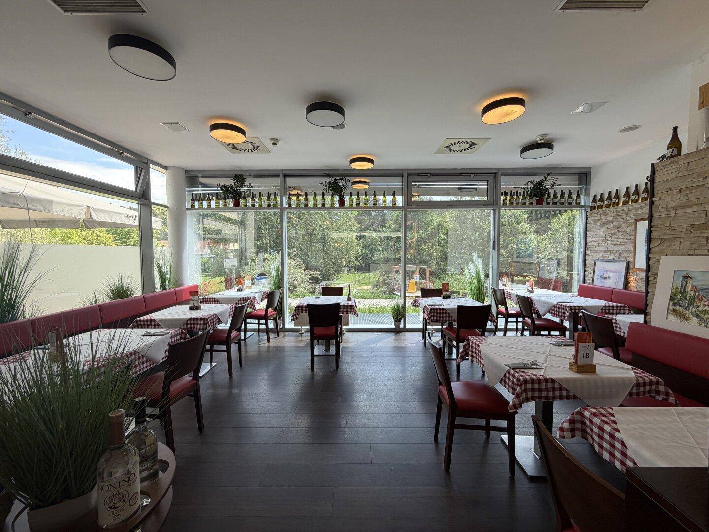 Heller Restaurantraum mit großen Fenstern, roten Sitzbänken und Blick ins Grüne.