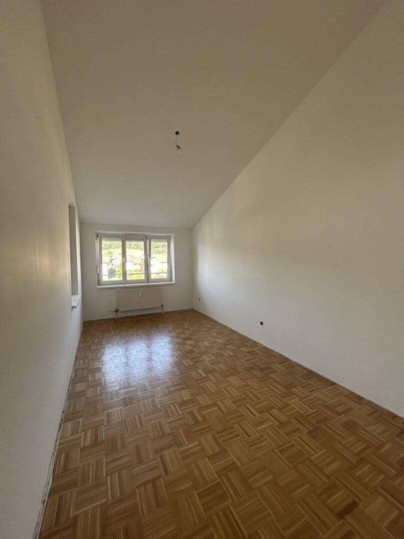 Leeres Zimmer mit Parkettboden, weißen Wänden, einem Fenster und einer Dachschräge.