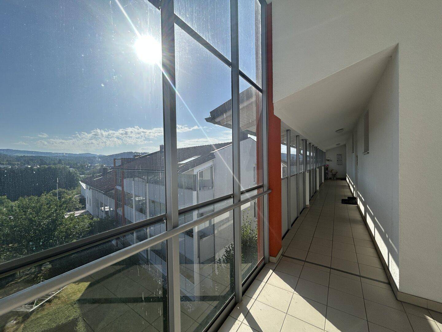 Heller Flur mit großer Glasfassade, Fliesenboden und sonnigem Ausblick auf die Umgebung.