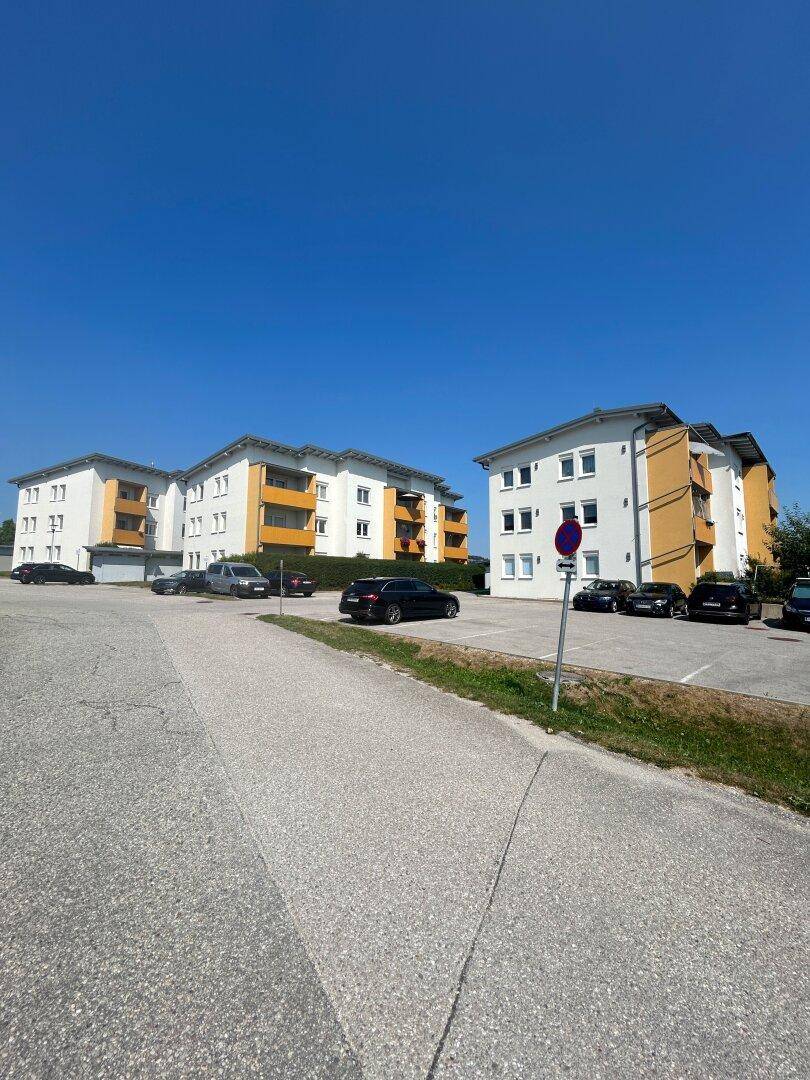 Mehrere moderne Wohngebäude mit gelben Akzenten und Parkplätzen unter blauem Himmel.