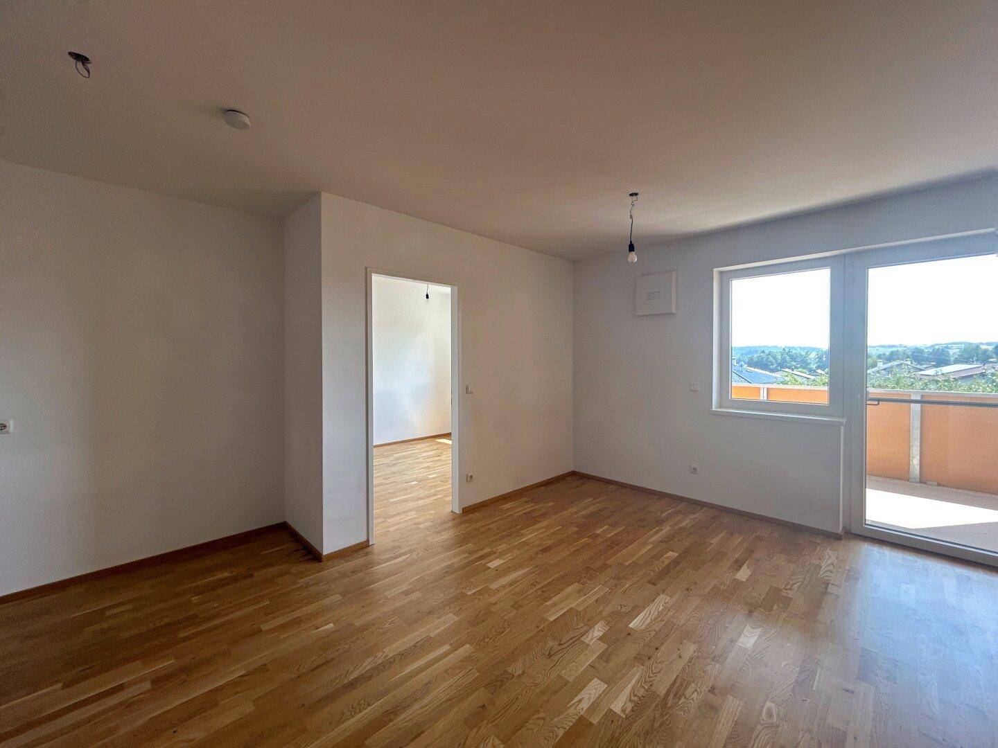 Heller Wohnraum mit Parkettboden und Zugang zu einem Balkon, ideal für offenes Wohnen.
