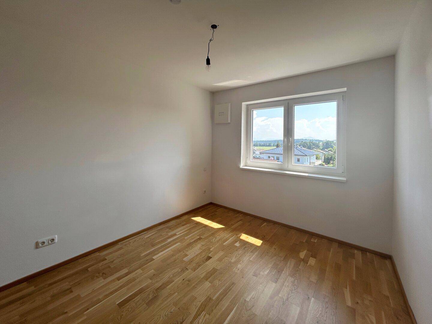 Ruhiges Schlafzimmer mit Parkettboden und Fenster, das viel Tageslicht hereinlässt.