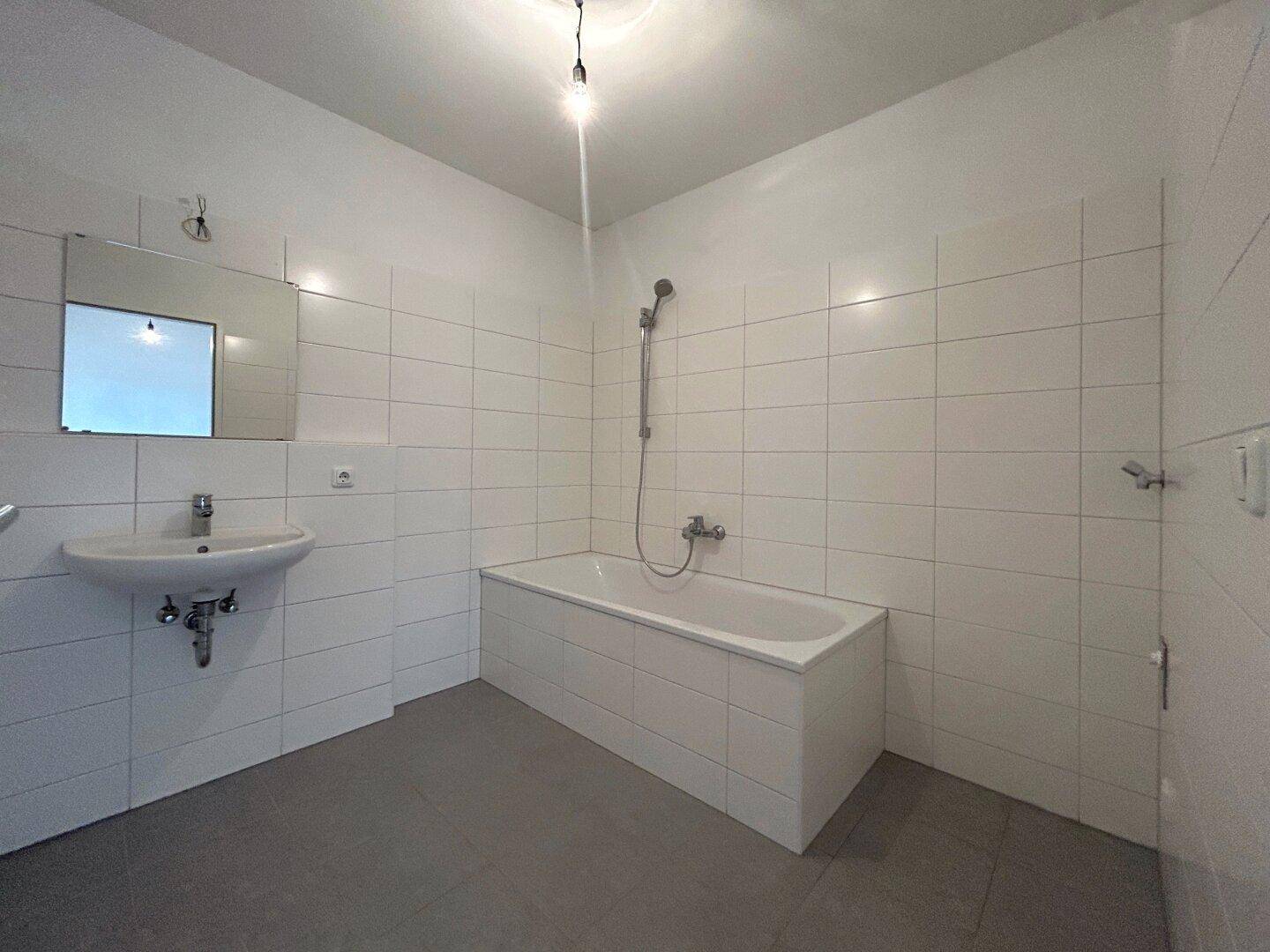 Funktionales Badezimmer mit Badewanne, Waschbecken und weißen Fliesen, in gutem Zustand.