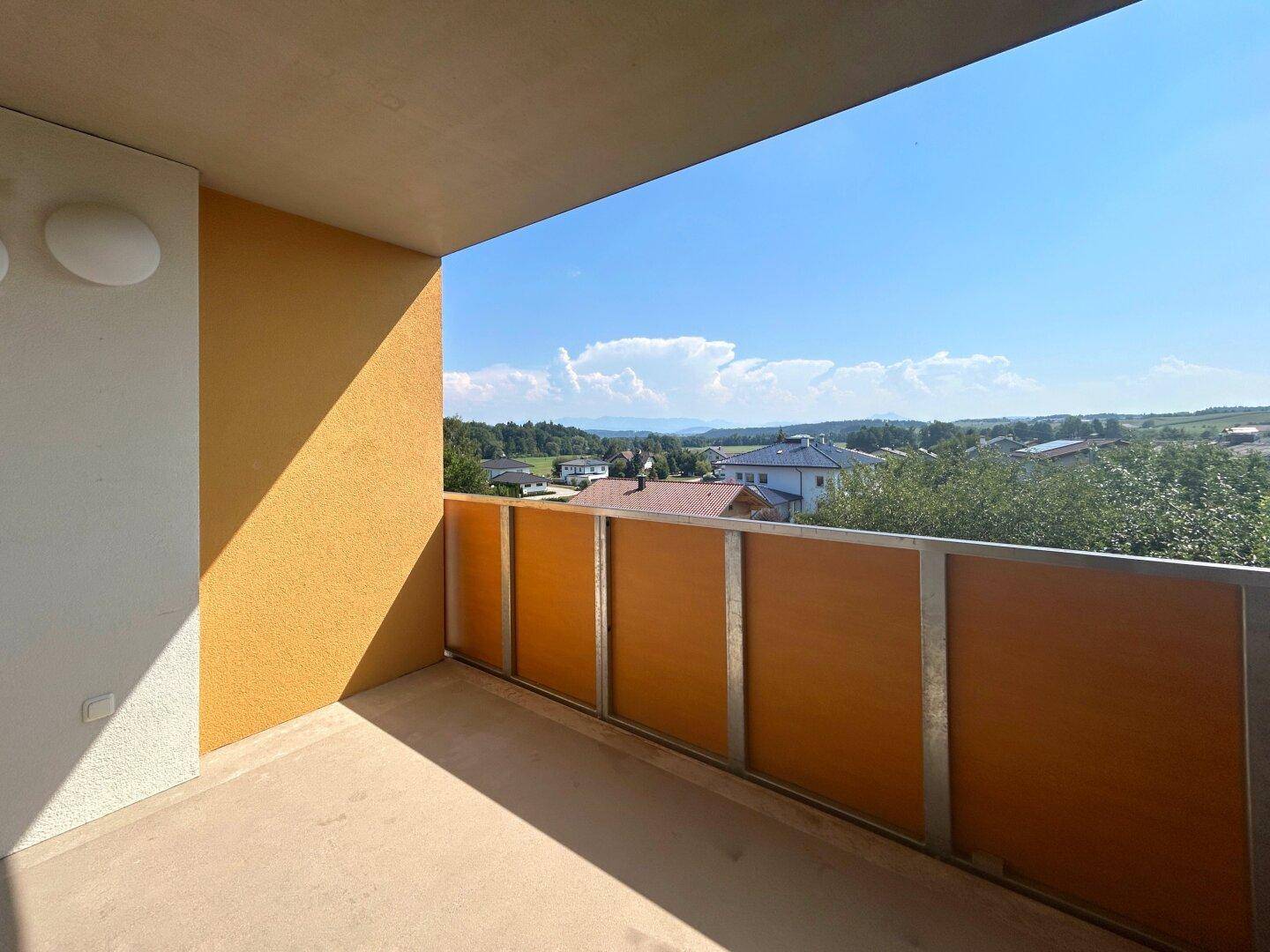 Geräumiger Balkon mit weitem Blick über die Landschaft und umliegende Häuser unter blauem Himmel.