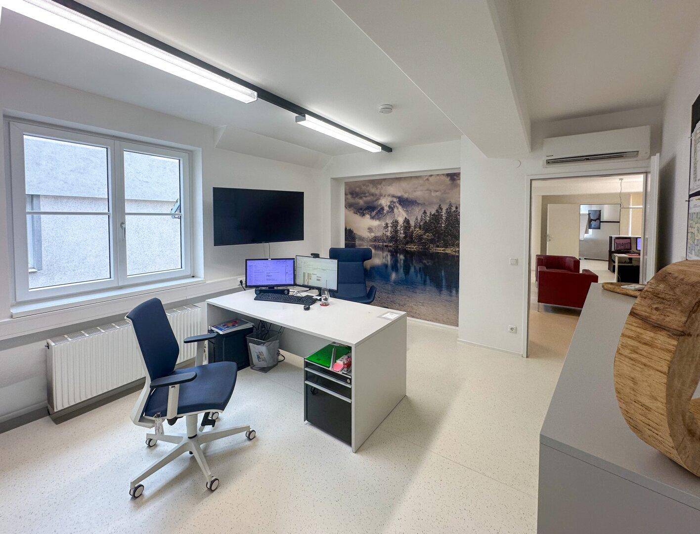 Geräumiges Büro mit Schreibtisch, Bürostuhl, Wandbild und Klimaanlage.