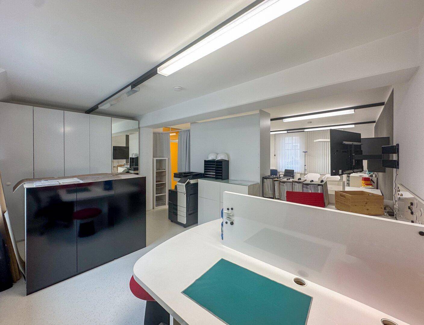Großes Büro mit mehreren Arbeitsplätzen, Drucker und Blick in den Flur.