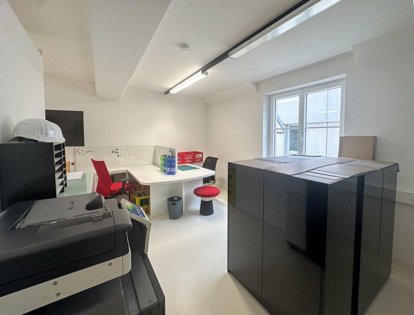 Helles Büro mit großem Schreibtisch, Drucker und Fensterblick.