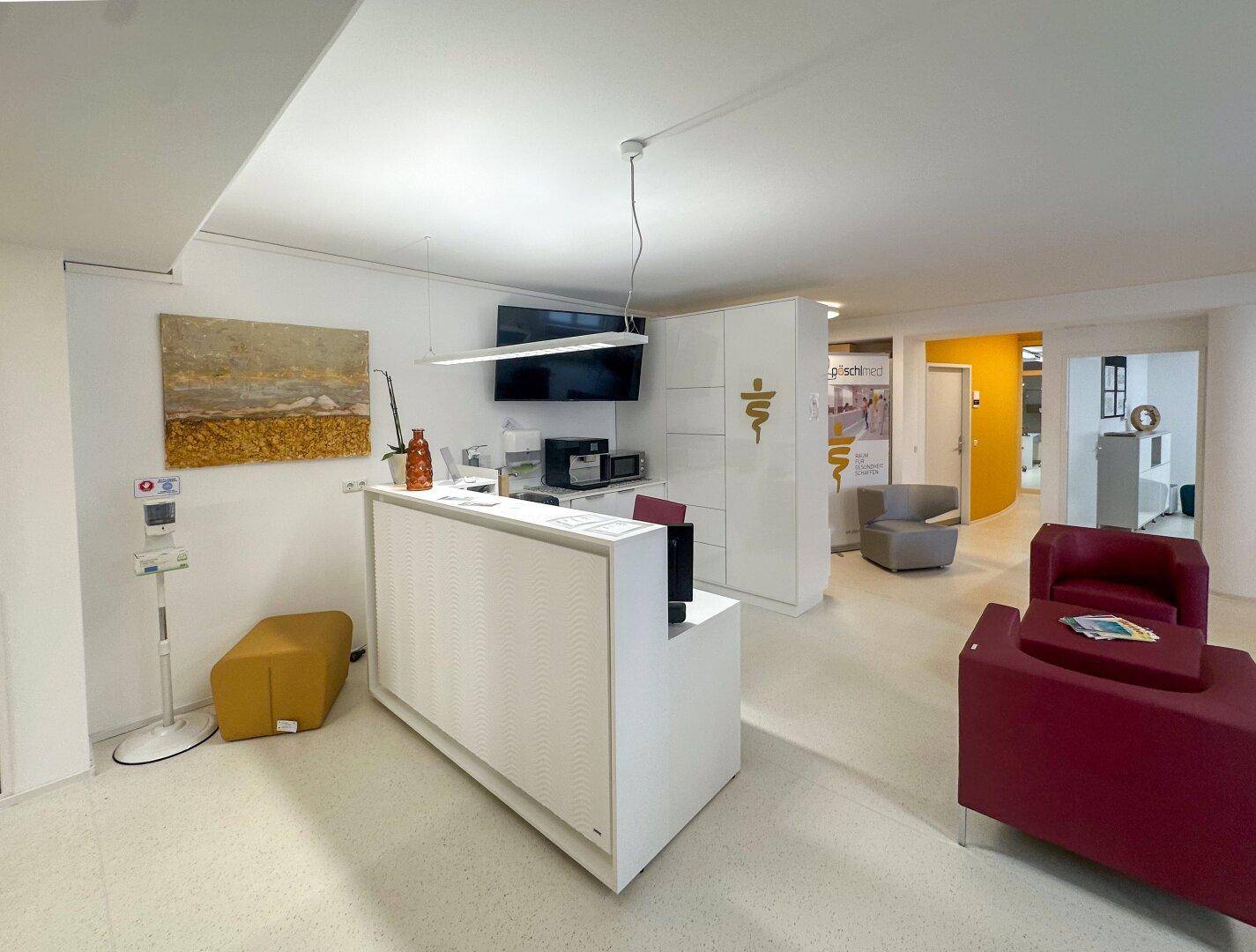 Moderner Empfangsbereich mit weißer Rezeptionstheke, Sitzgelegenheiten und Kunst an der Wand.
