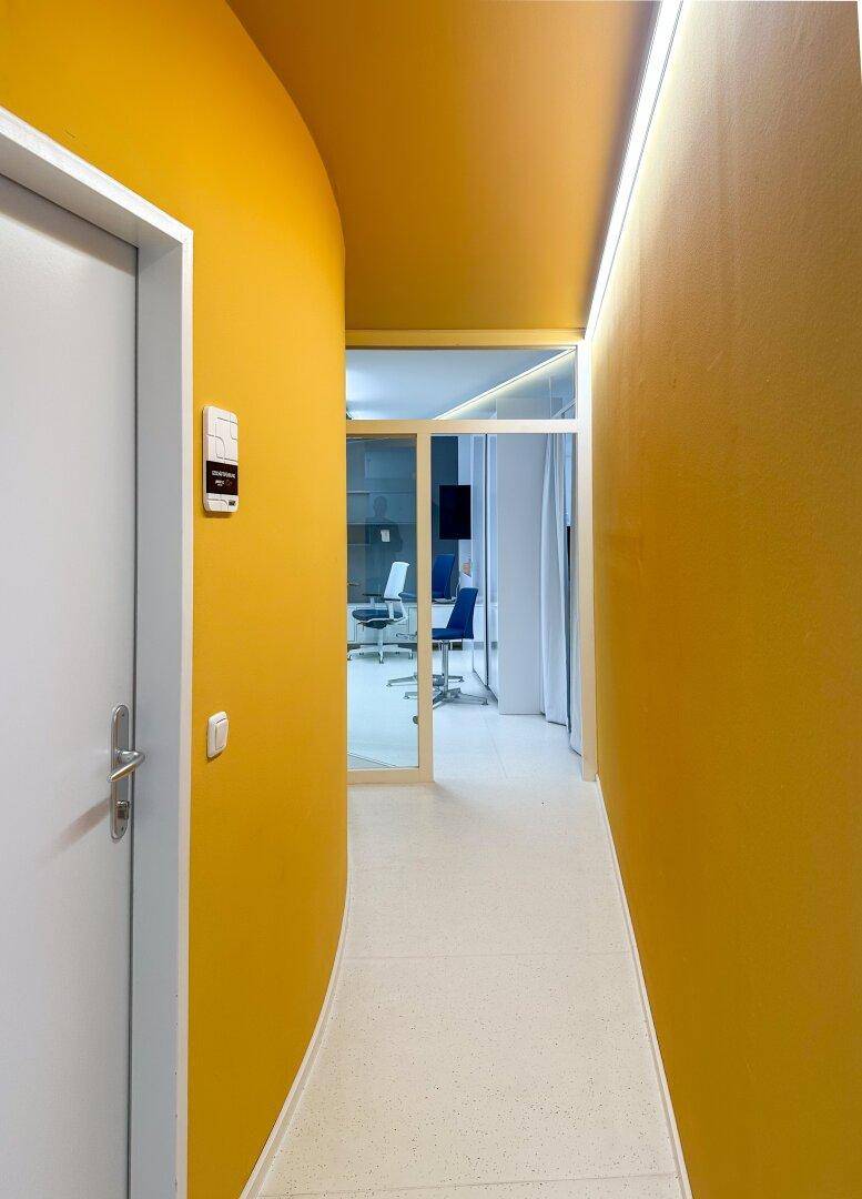 Heller Flur mit gelben Wänden und Blick in ein weiteres Büro.