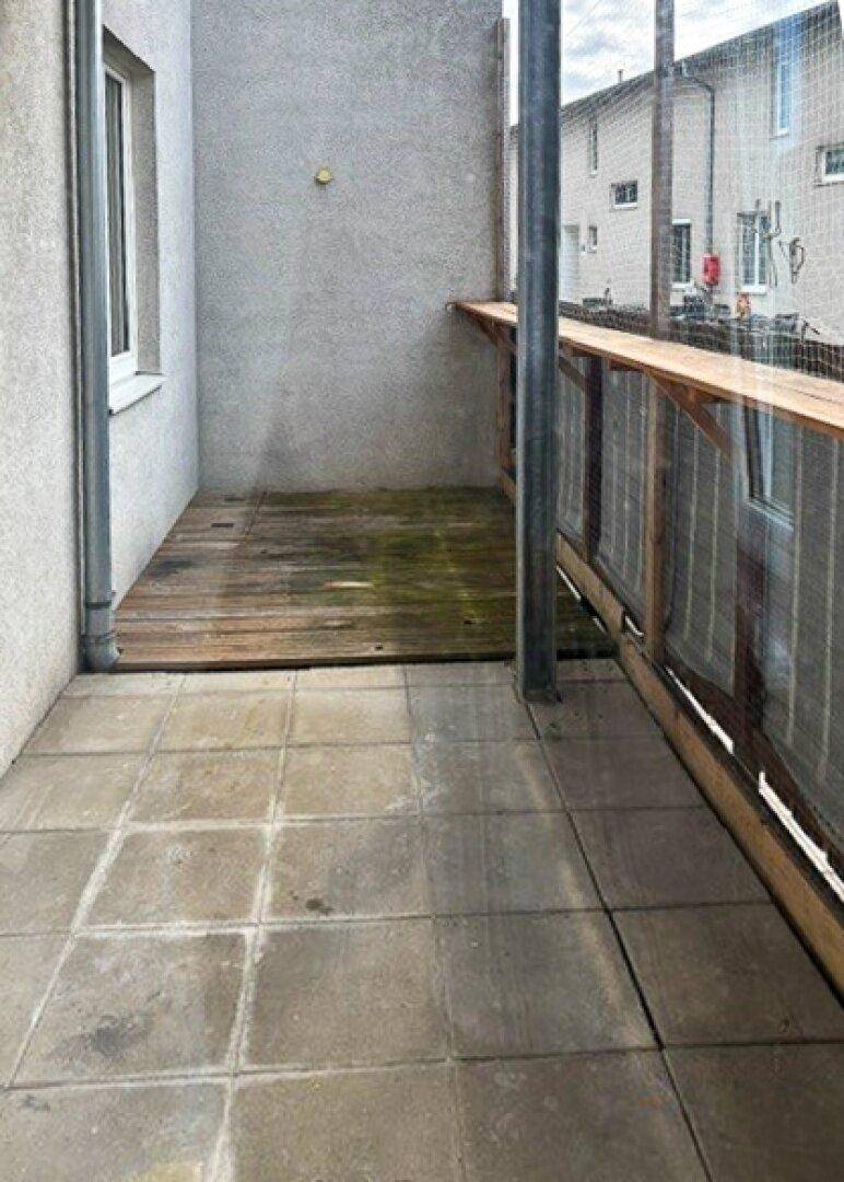 Kleiner Balkon mit Fliesenboden und Holzdetails, umgeben von einer schützenden Umzäunung.