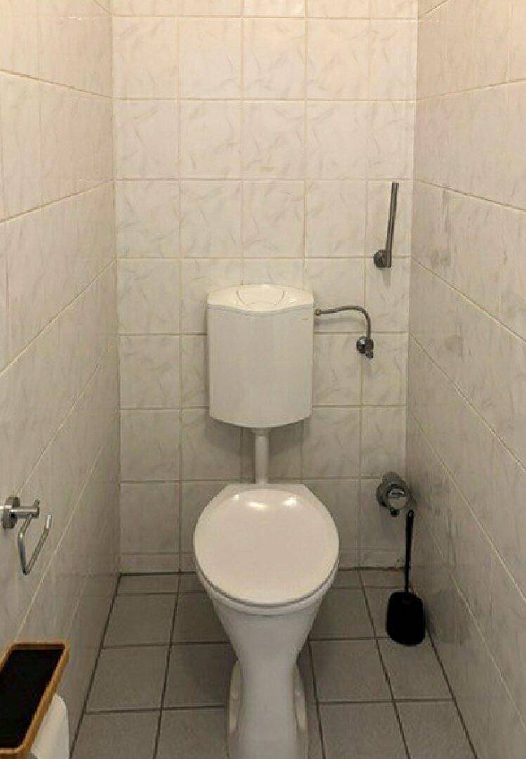 Separate Toilette mit weißen Fliesen an Wänden und Boden.