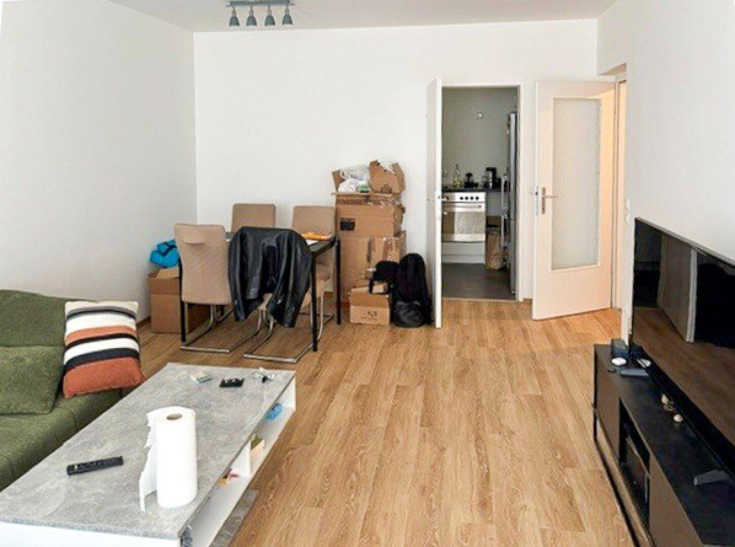 Wohnbereich mit Laminatboden, einem Sofa und Blick durch eine offene Tür in die Küche.