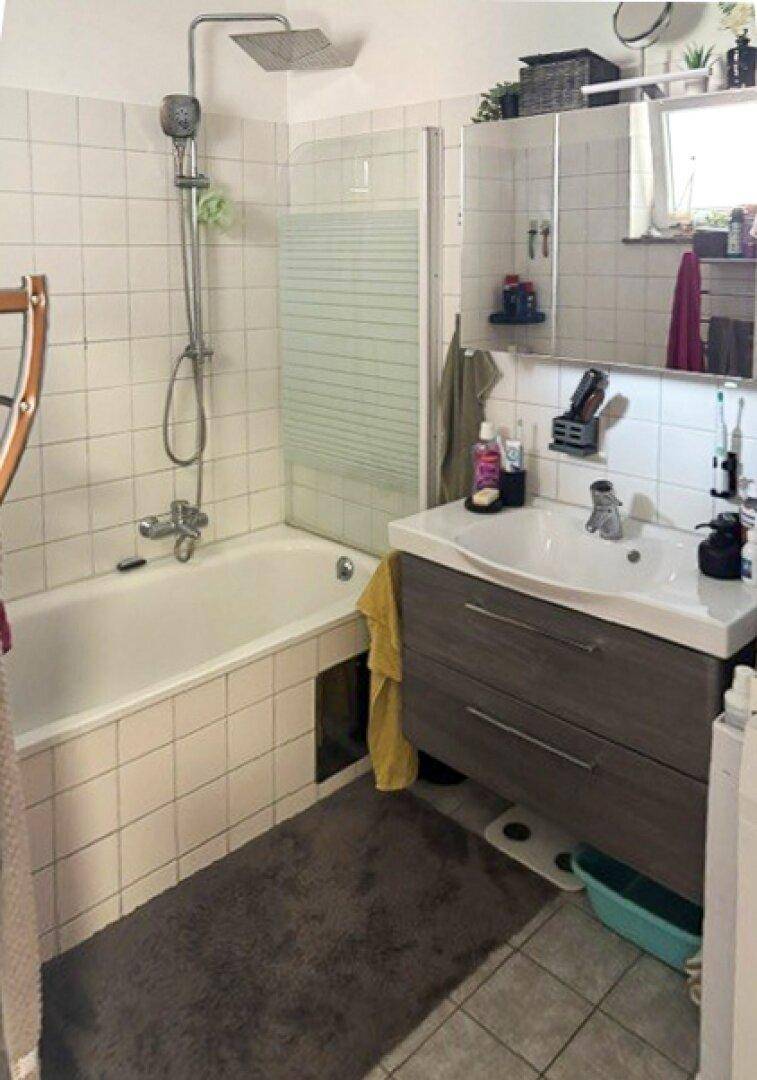 Badezimmer mit Badewanne, Duschfunktion, modernem Waschtisch und einem Fenster für natürliche Belüftung.