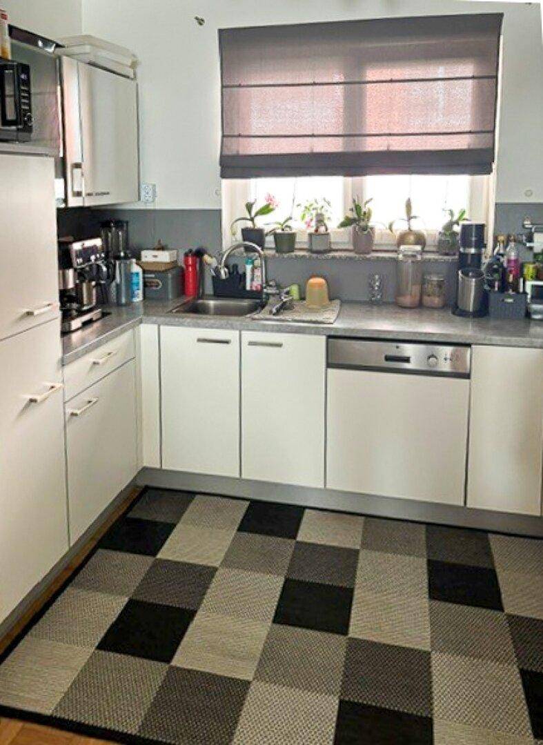 Funktionale Küche mit weißen Schränken, integriertem Geschirrspüler und einem Fenster über der Spüle.