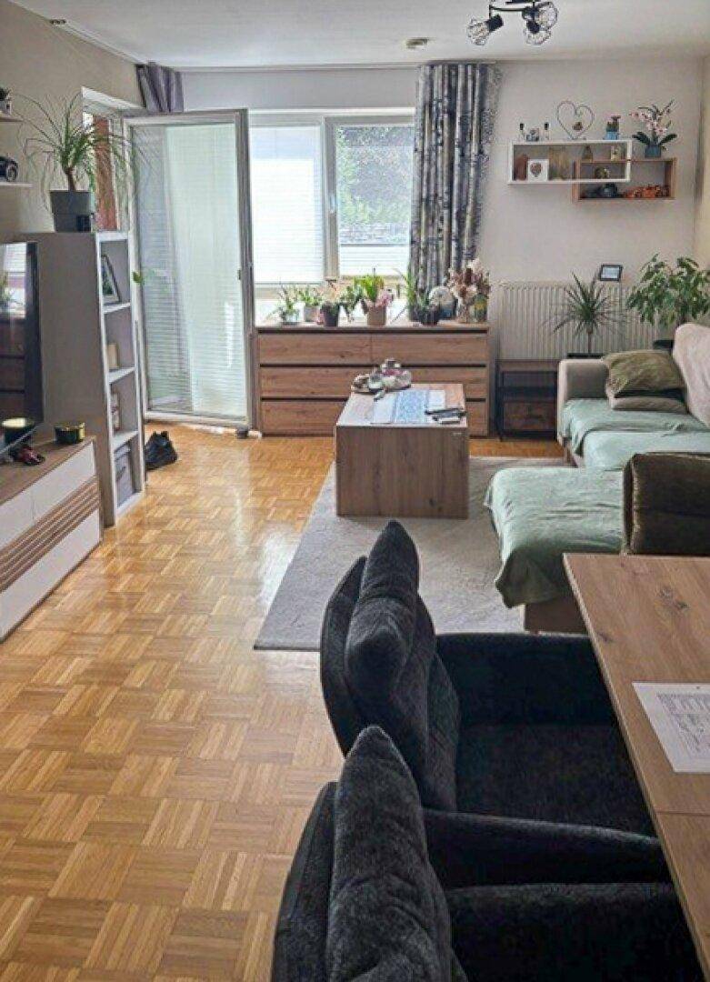 Helles Wohnzimmer mit Parkettboden, gemütlicher Sitzecke und Zugang zu einem Balkon oder einer Terrasse.