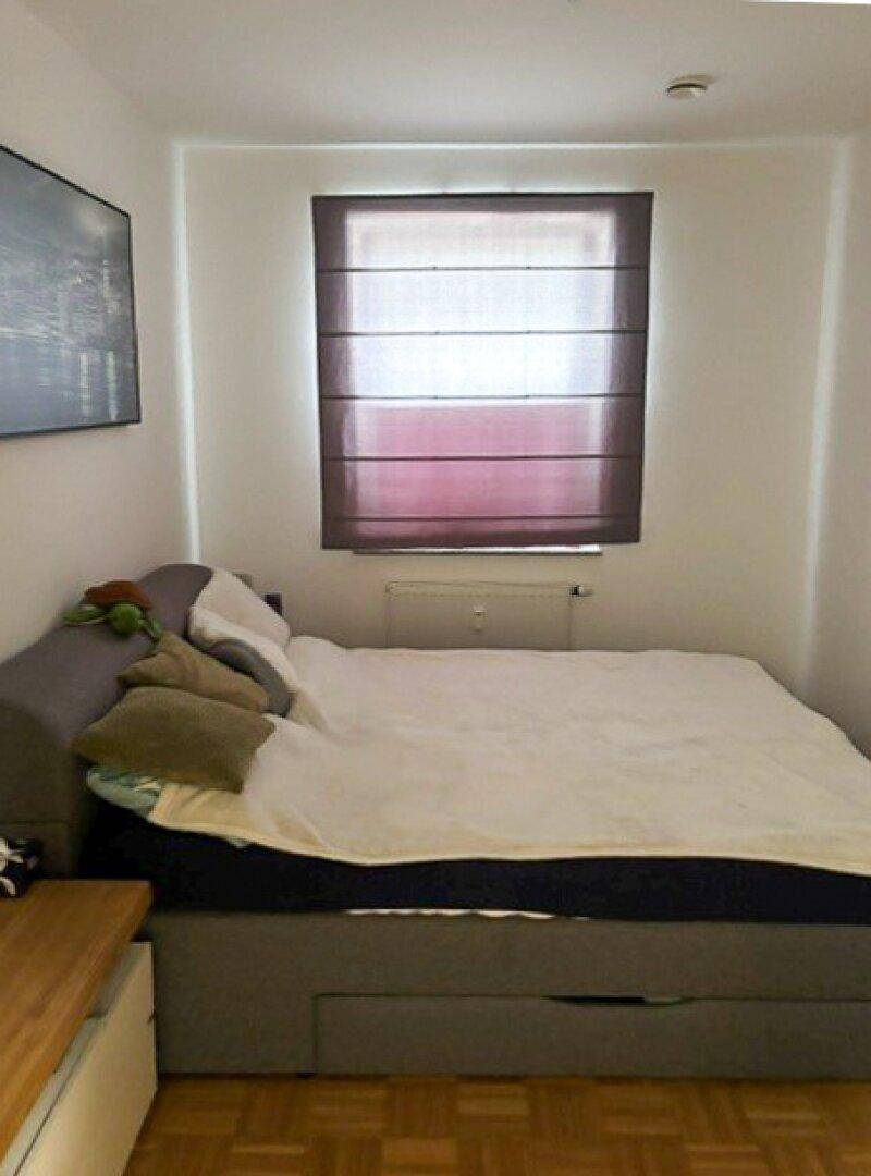 Gemütliches Schlafzimmer mit einem Bett, Holzparkett und einem Fenster mit blickdichtem Rollo.