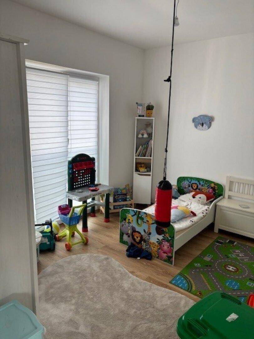 Kinderzimmer mit kleinem Bett, Spielzeug und einem großen Fenster für viel Tageslicht.
