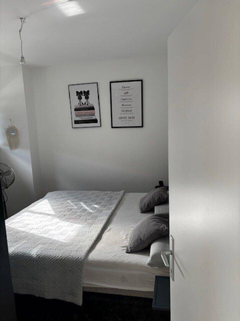 Schlafzimmer mit Bett, gerahmten Bildern an der Wand und einem Ventilator.