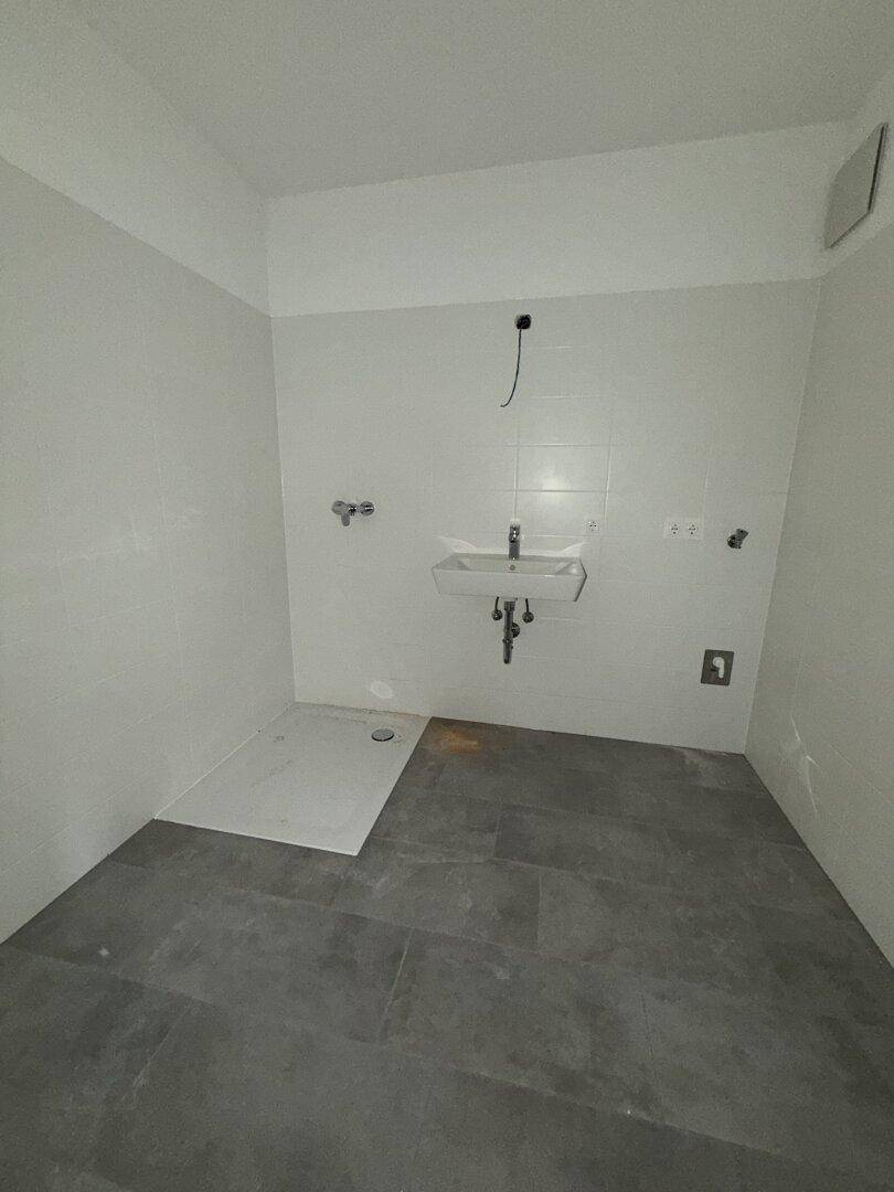 Modernes Badezimmer mit Duschwanne, Waschbecken und weißen Fliesen an den Wänden. Der Raum ist noch unmöbliert.