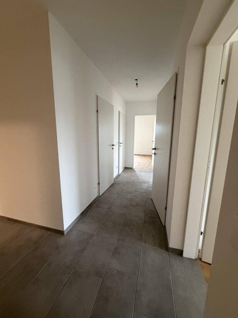 Langer, leerer Flur mit dunklen Fliesen und mehreren weißen Türen. Der Bereich ist gut beleuchtet.