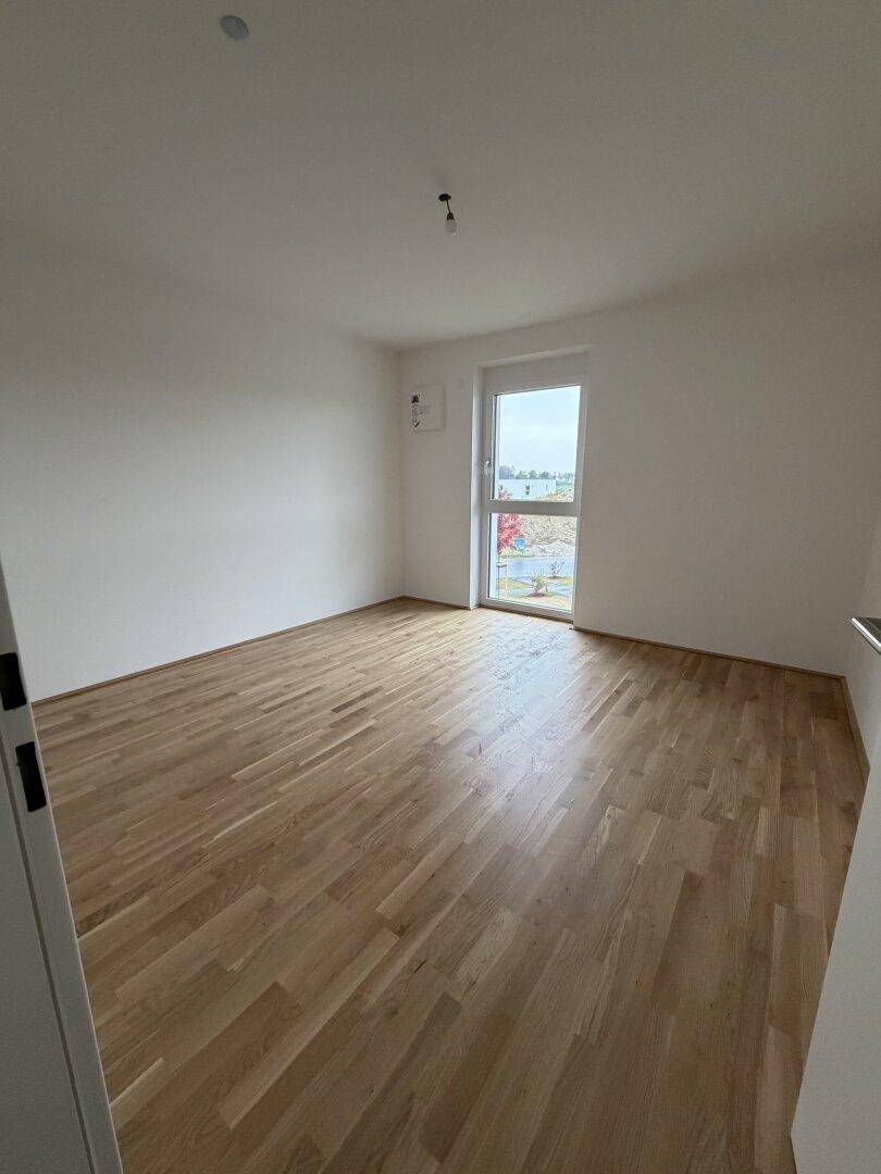 Heller, leerer Raum mit Holzboden und einem Fenster mit Blick nach draußen. Perfekt für ein Kinderzimmer.