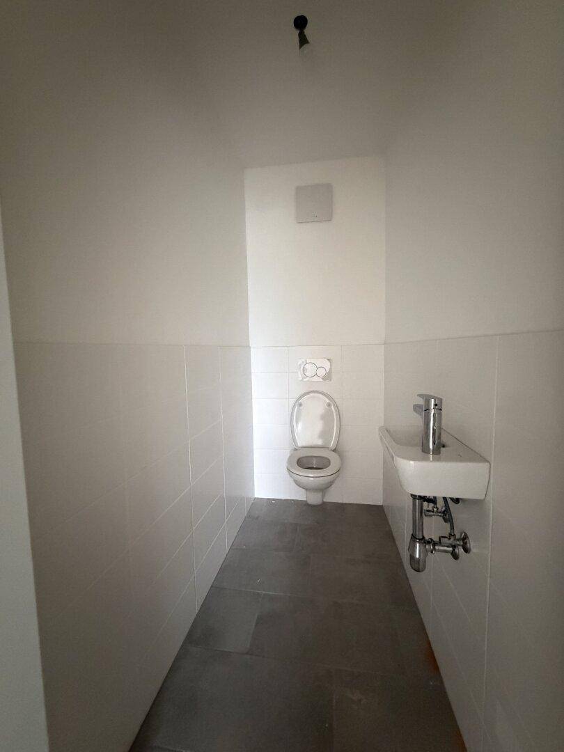 Kleines Gäste-WC mit Toilette, Waschbecken und weißen Wandfliesen. Der Boden ist mit dunklen Fliesen versehen.