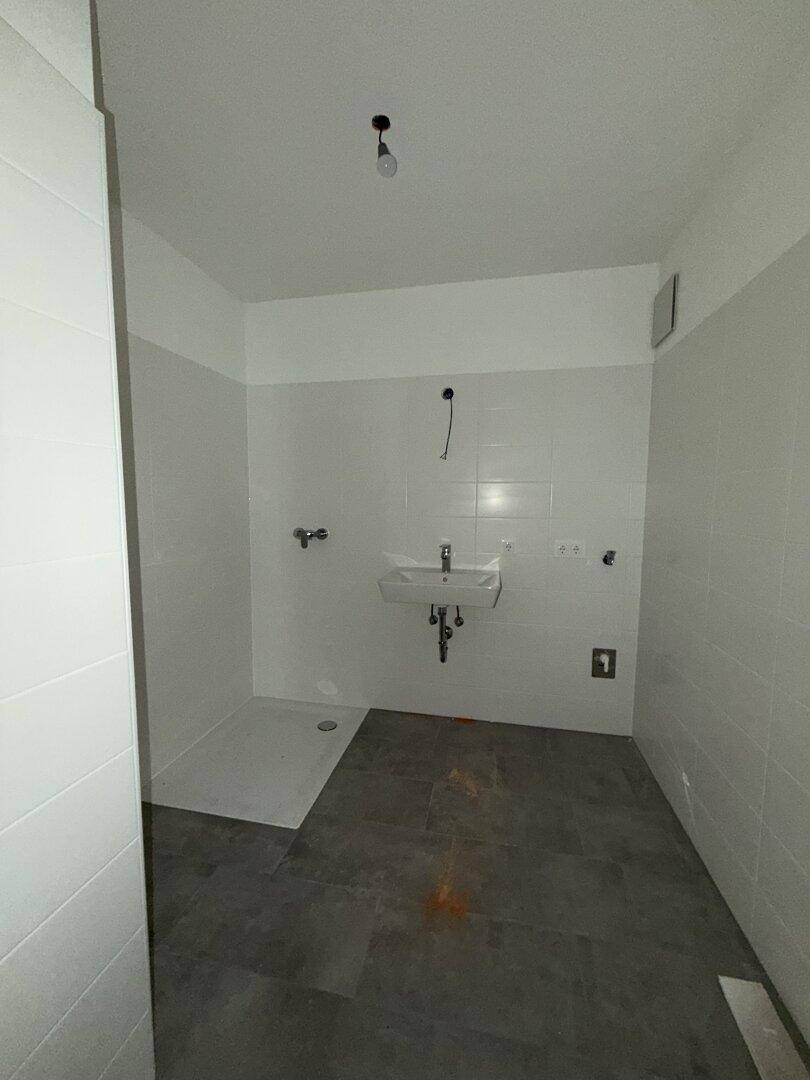 Modernes Badezimmer mit weißen Fliesen, grauem Boden und einer ebenerdigen Dusche sowie einem Waschbecken.