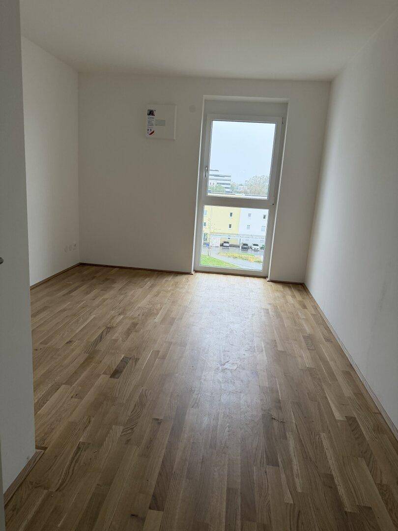 Weiteres leeres Zimmer mit Parkettboden und einem hohen Fenster, ideal als Schlaf- oder Arbeitszimmer.
