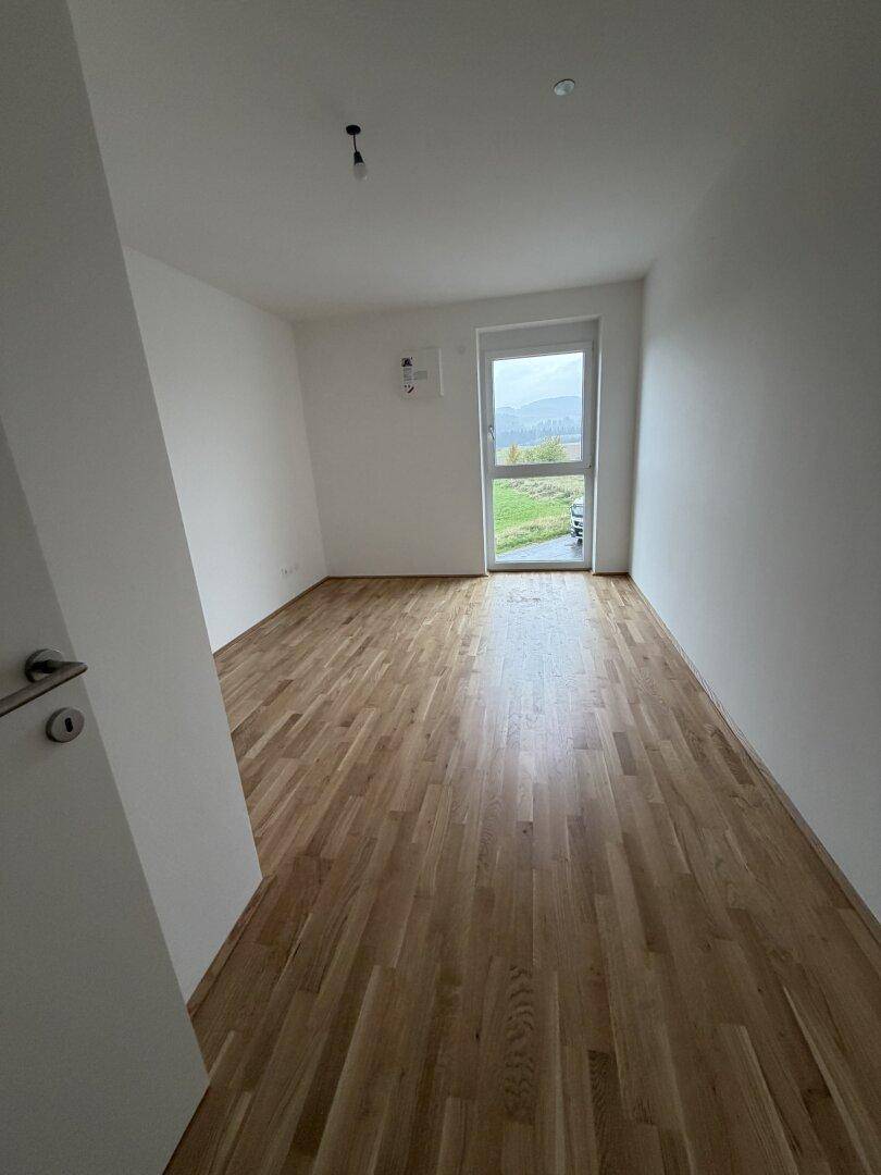 Weiteres helles Zimmer mit Parkettboden und Ausblick in die Landschaft.