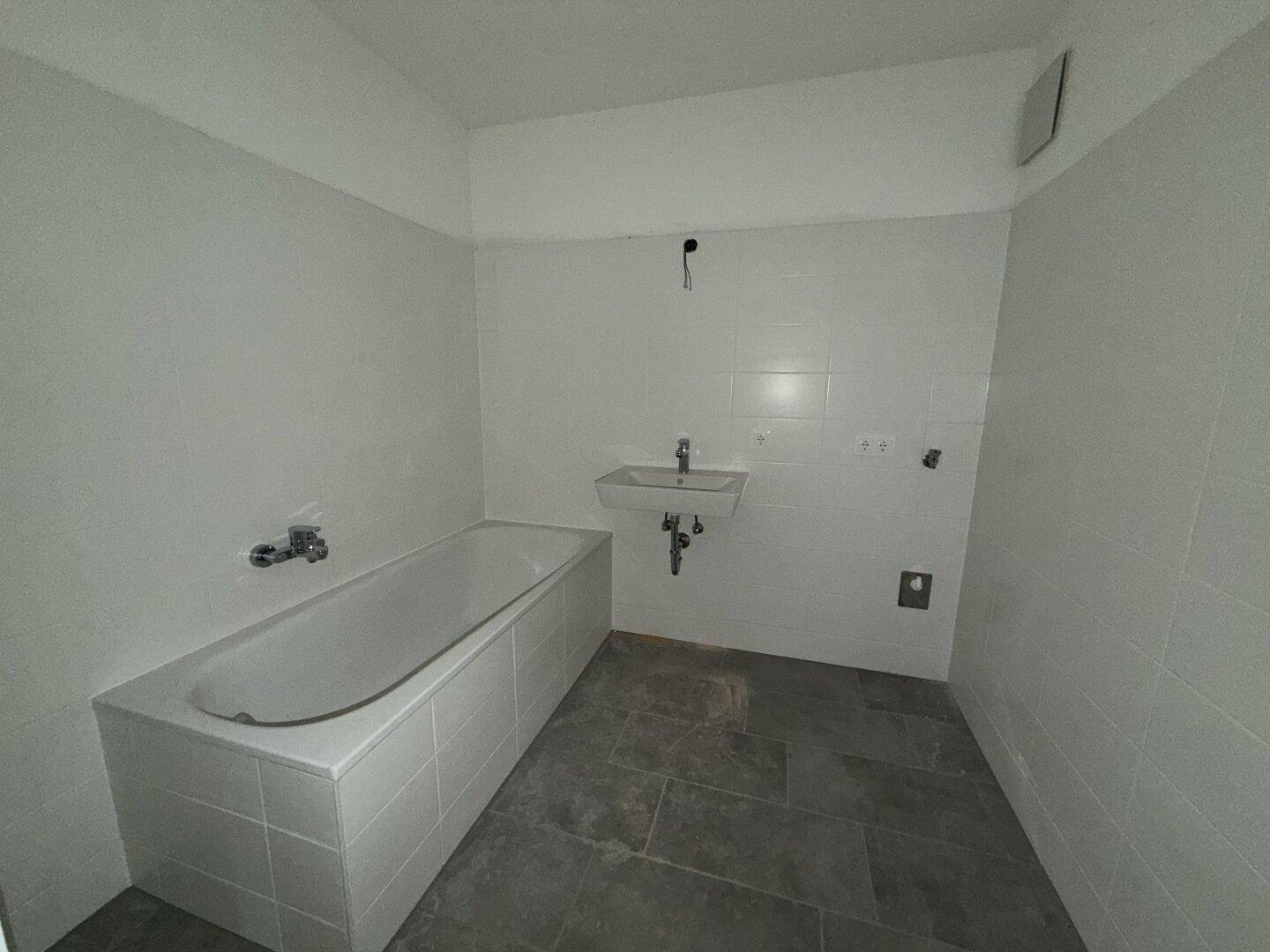 Modernes Badezimmer mit Badewanne, Waschbecken und grauen Fliesen.