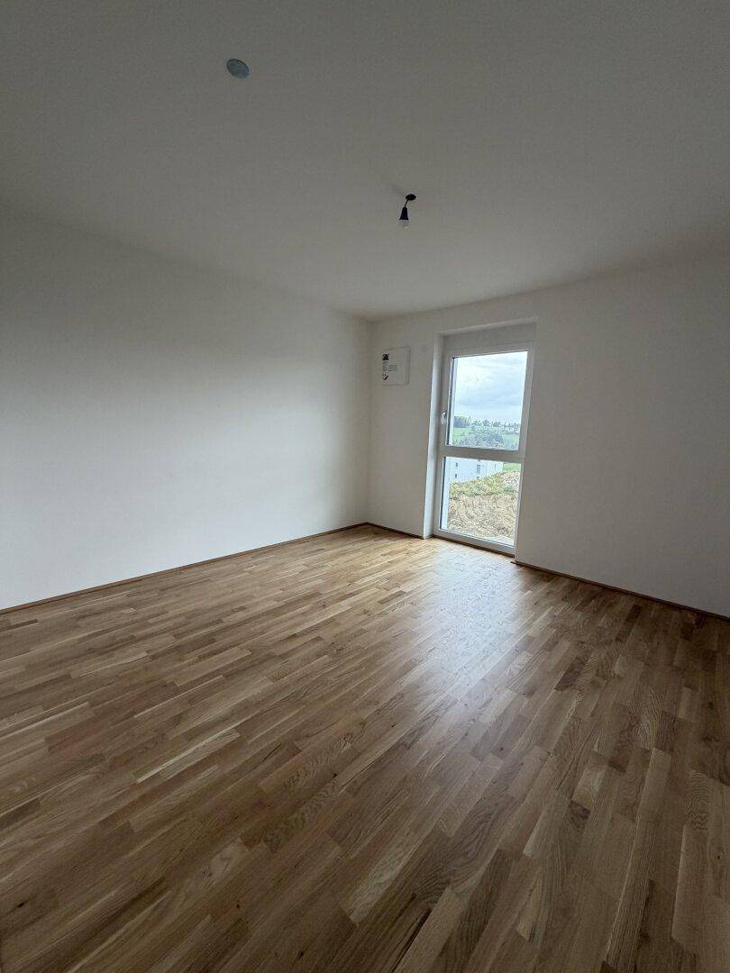 Helles Zimmer mit neuem Parkettboden und Fenster mit Blick ins Grüne.