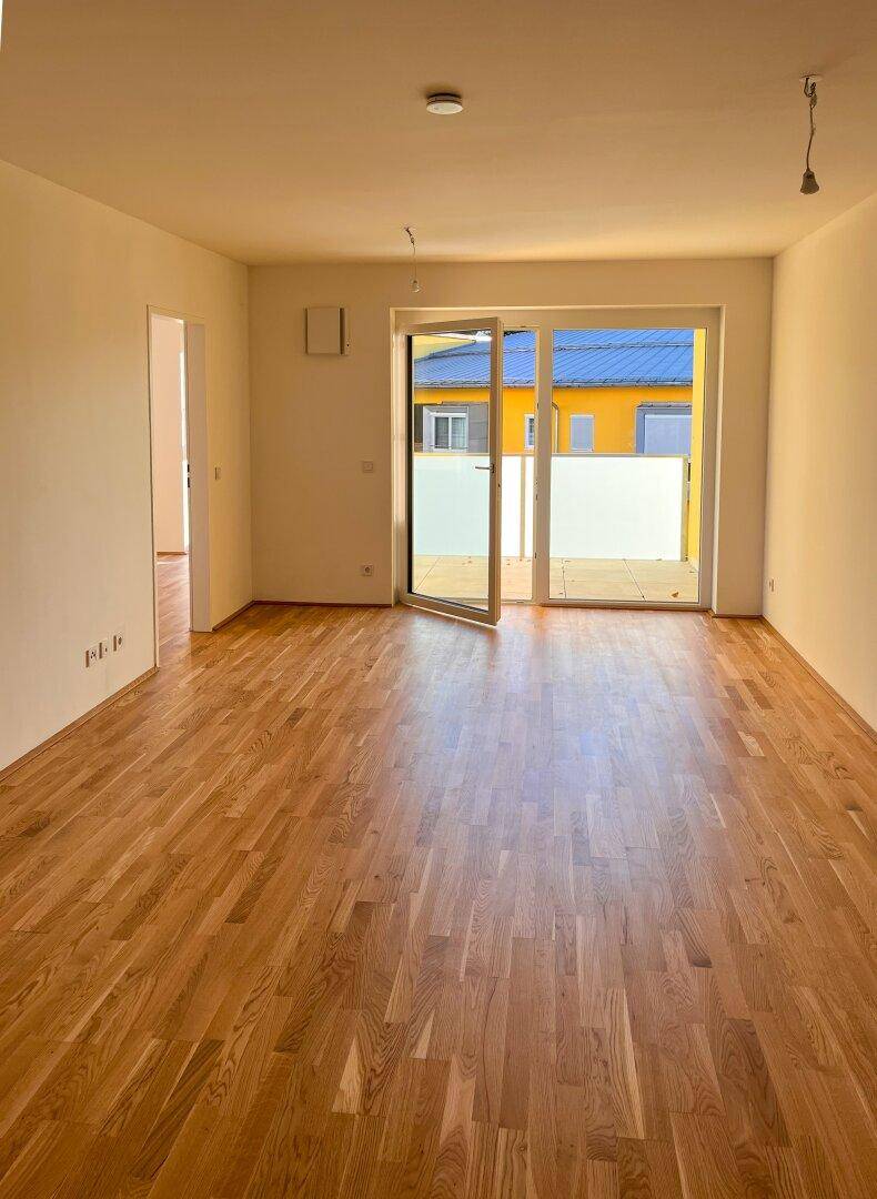 Helles Wohnzimmer mit Parkettboden und Zugang zu einer Terrasse oder einem Balkon.