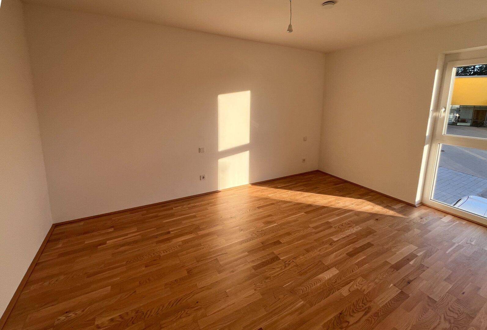 Helles Schlafzimmer mit Parkettboden und viel natürlichem Licht durch das große Fenster.