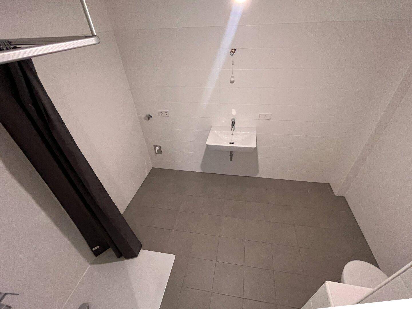 Modernes Badezimmer mit weißen Fliesen, grauen Bodenfliesen, wandhängendem Waschbecken und Dusche.