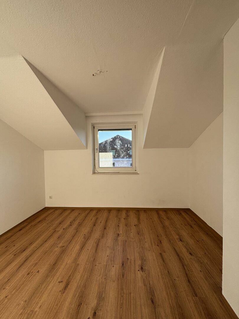 Helles Dachzimmer mit Laminatboden, schrägen Decken und Fenster mit Bergblick.