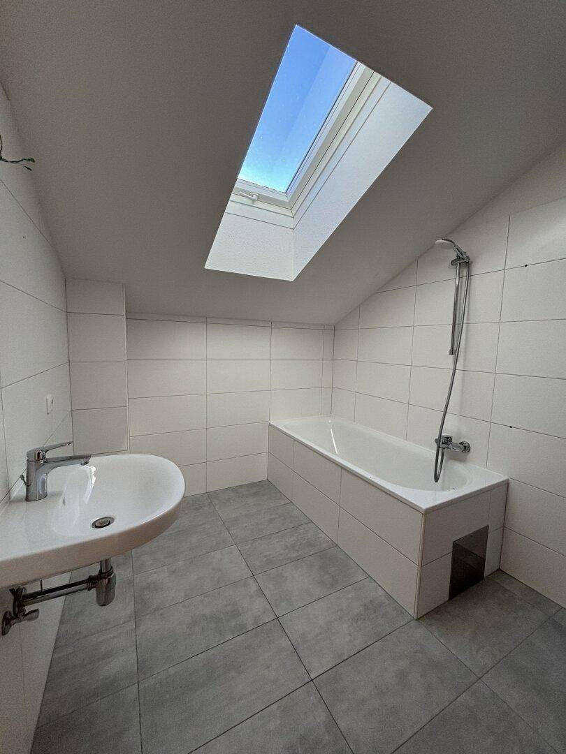 Modernes Badezimmer mit Badewanne, Waschbecken, Fliesen und großem Dachfenster.