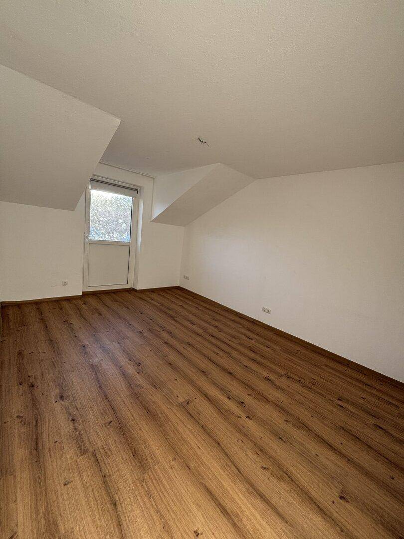 Geräumiges Dachzimmer mit Laminatboden, schrägen Decken und Fenster.