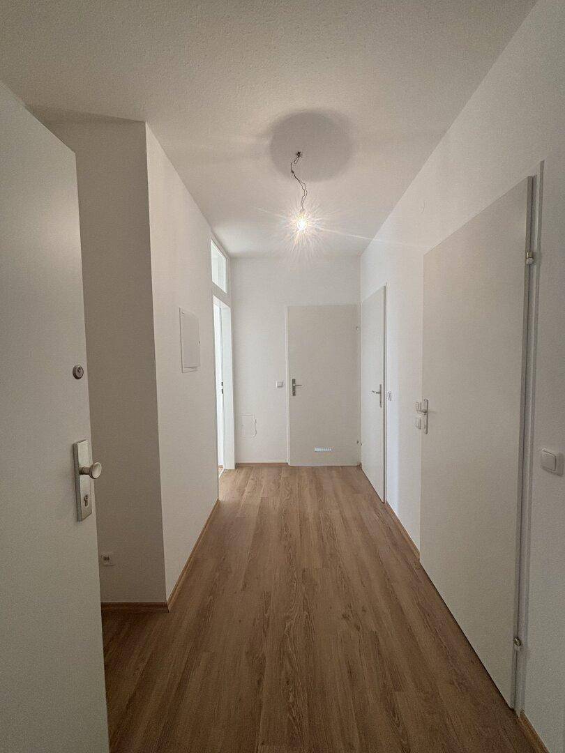 Heller Flur mit Laminatboden und weißen Wänden, der zu verschiedenen Räumen führt.