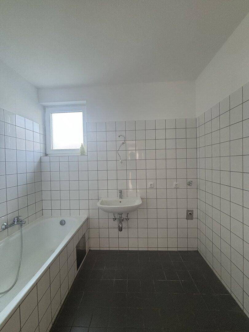 Funktionales Badezimmer mit weißen Wandfliesen, Badewanne, Waschbecken und Fenster.