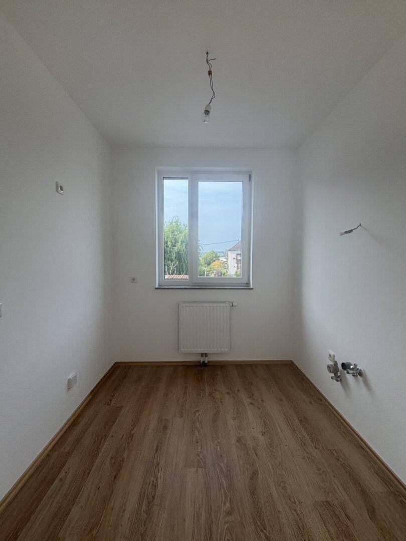 Leerer Raum mit Laminatboden und Anschlüssen, vorbereitet für eine Küche oder Waschküche.