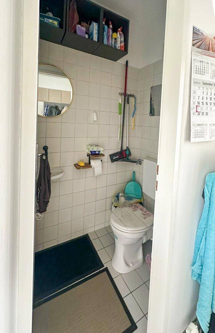 Kleines Gäste-WC mit weißen Fliesen, Toilette und kleinem Waschbecken.