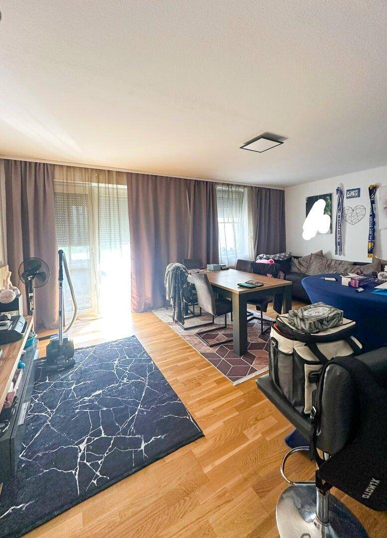 Geräumiger Wohn-Essbereich mit Holzboden, dunklen Vorhängen und Zugang zum Balkon.