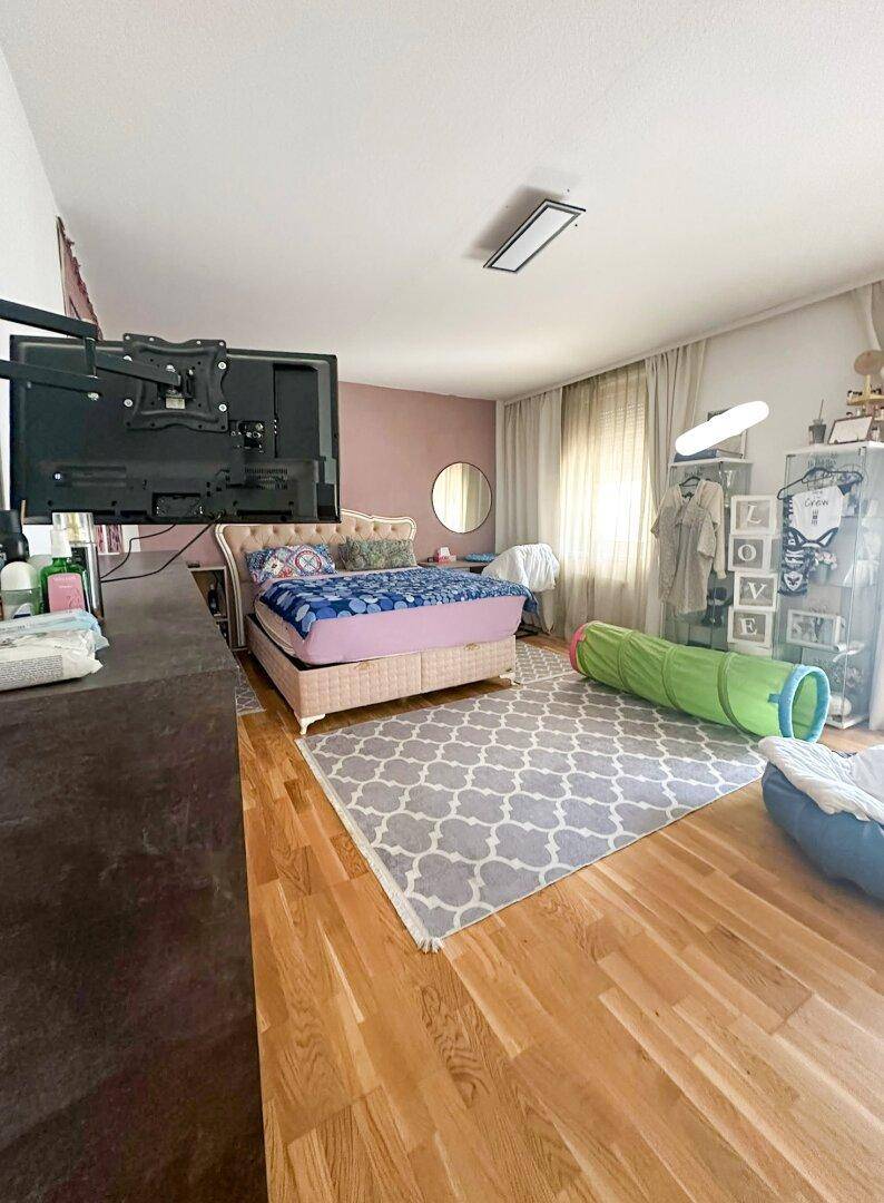 Helles Schlafzimmer mit Holzboden, großem Bett und einem Fernseher an der Wand.